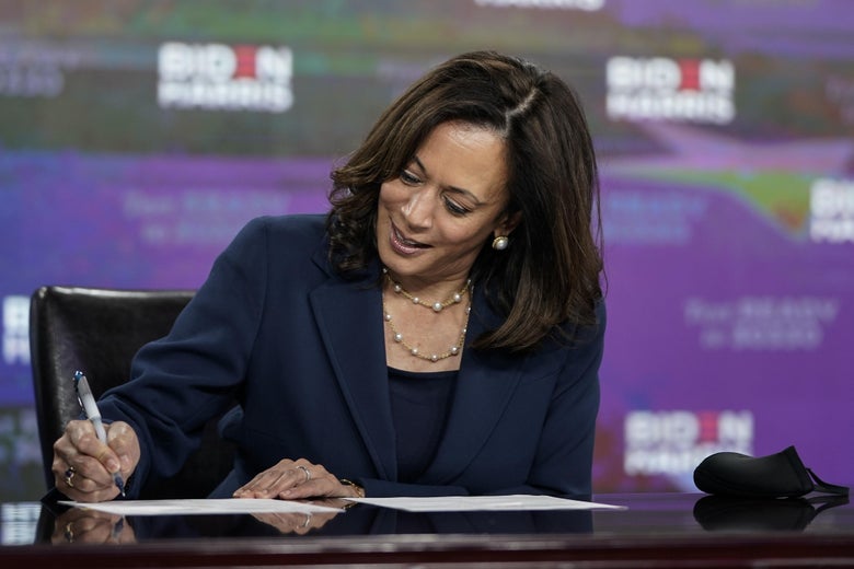 Kamala Harris smiles as she signs paperwork on a table