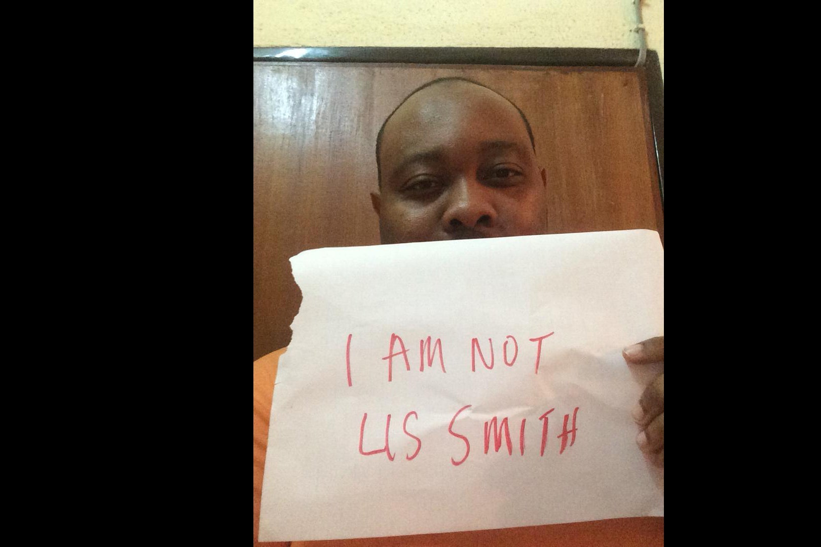Chinedu holds up a piece of paper that reads "I am not Lis Smith"