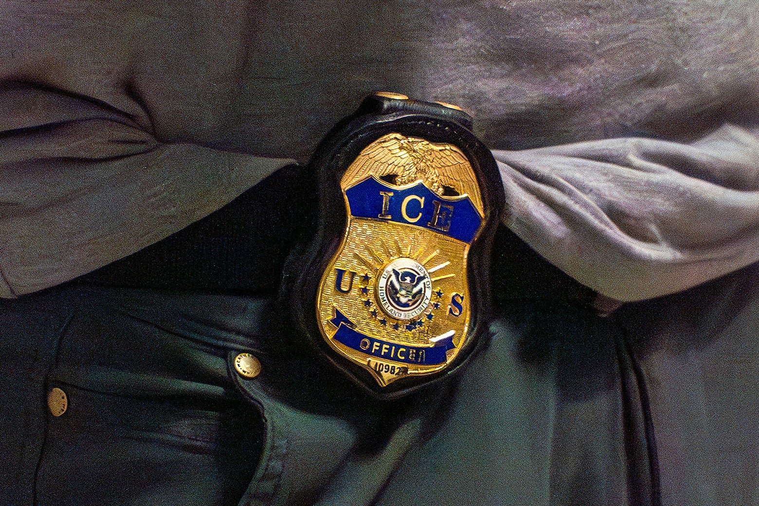 An ICE badge is on the waist of someone wearing a very sloppily tucked-in gray athletic tee and baggy black pants.