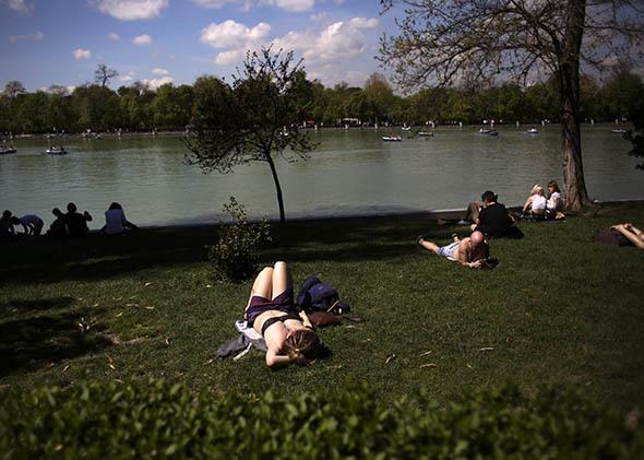 People sunbathe and watch boats on an artificial lake as they enjoy the warm weather during a sunny spring day at Madrid's Retiro park 