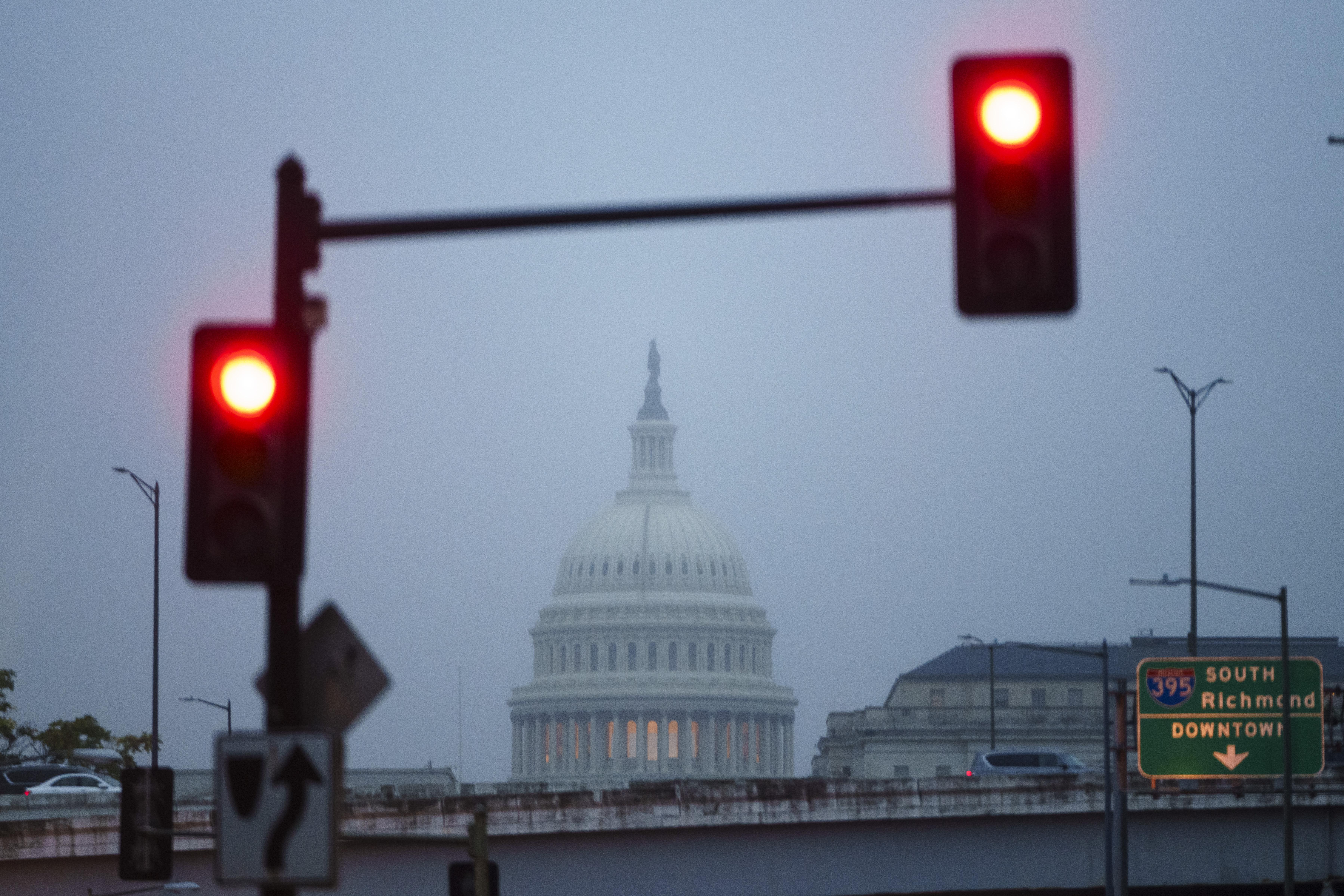 Capitol dome seen from a distance on a foggy morning, with red stoplights in the foreground
