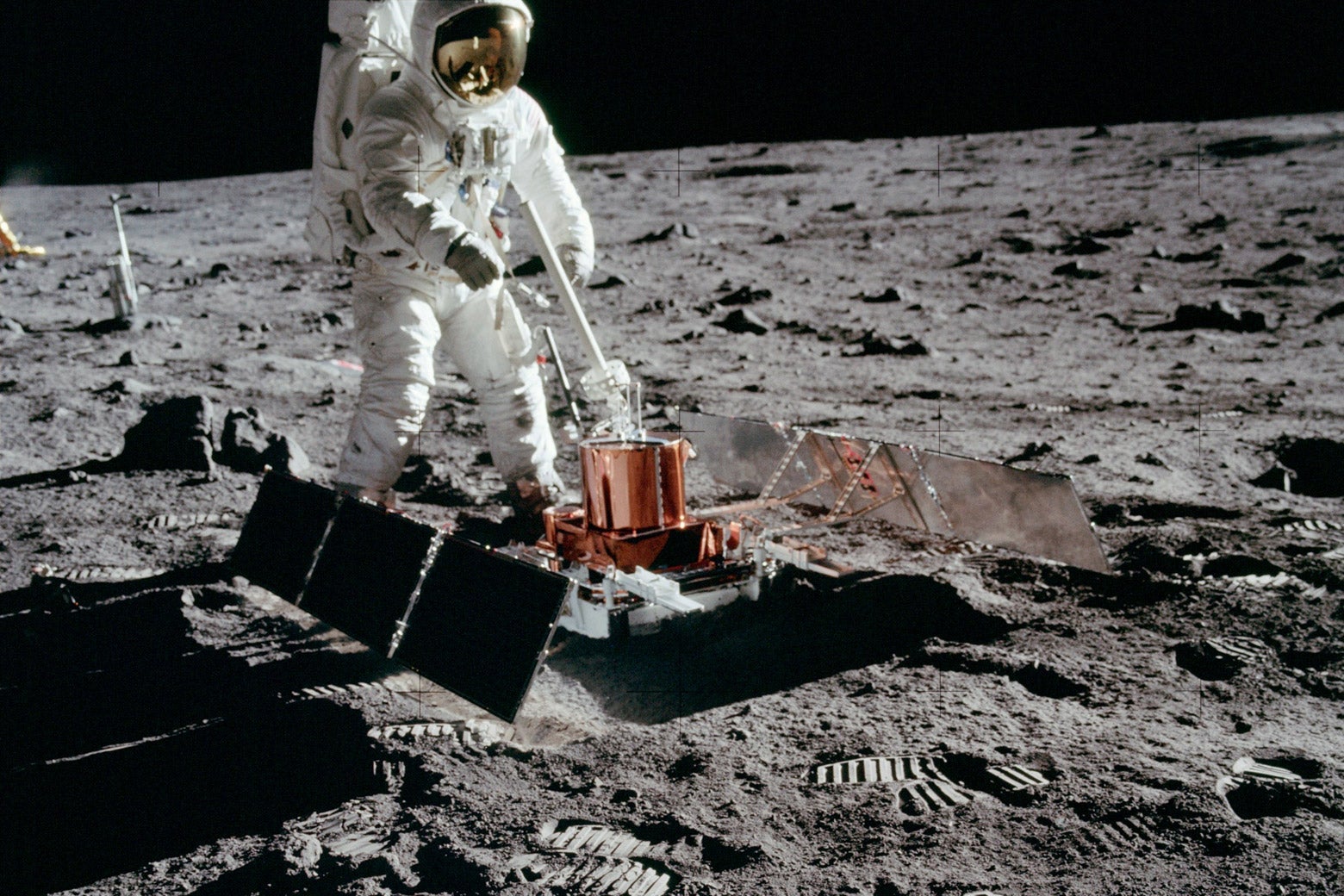 Apollo 11 astronaut Buzz Aldrin with the seismic experiment. Solar panels have deployed on the left and right and the antenna is pointed at Earth. The laser reflector is beyond the antenna and, in the distance, the TV camera is silhouetted against the black sky. 