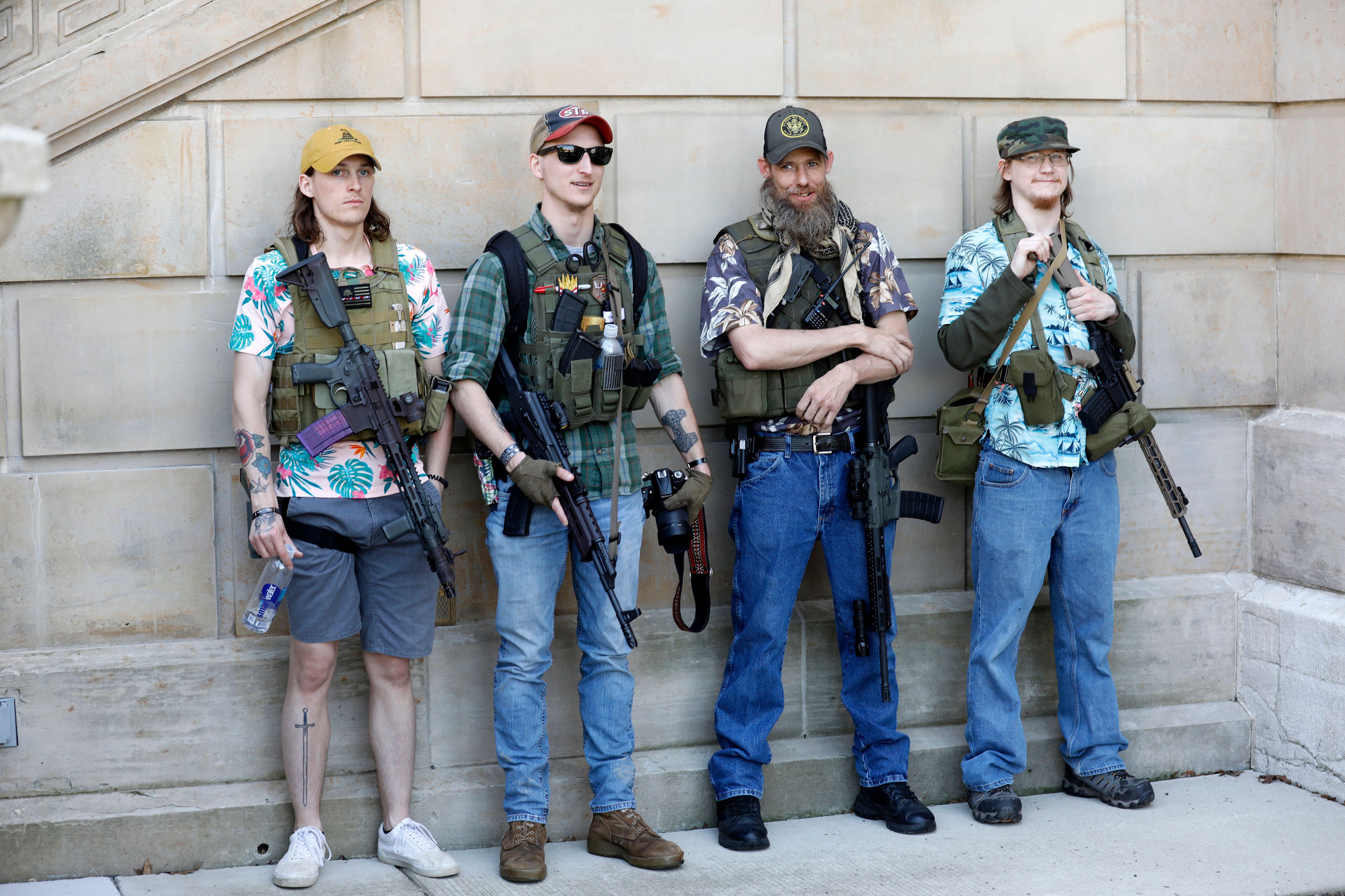Four Boogaloo Bois carrying rifles and wearing Hawaiian shirts, lined up against a wall.