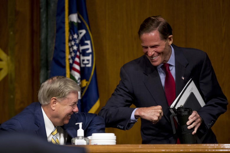 A seated Lindsey Graham elbow-bumps a standing Richard Blumenthal while both grin.