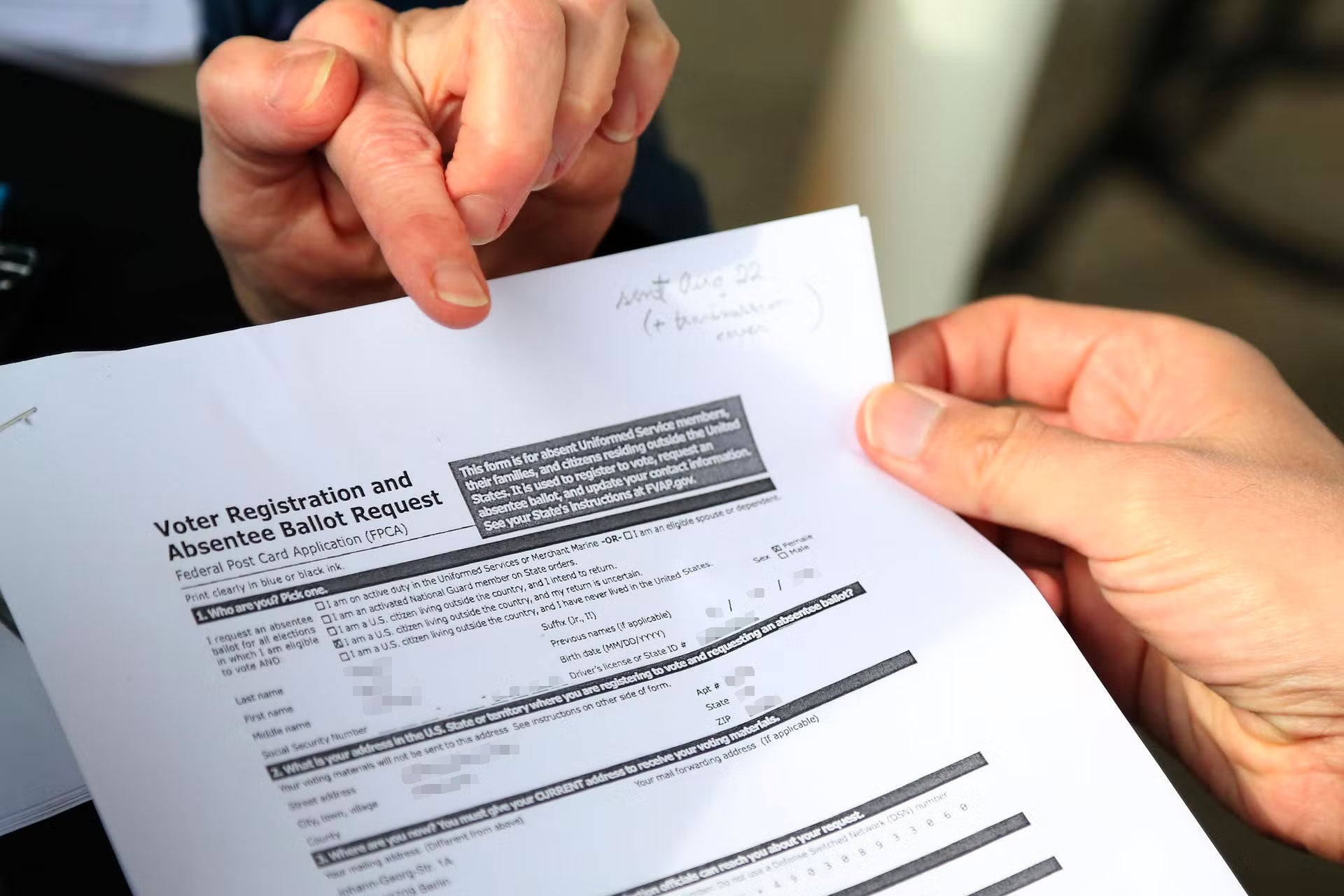 A finger points to a voter registration form being held by another person.