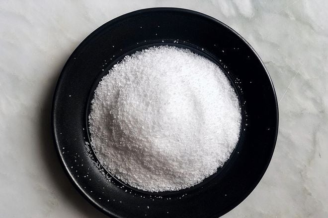 A pile of salt, pictured from above, on a black dish set against a gray marble countertop.