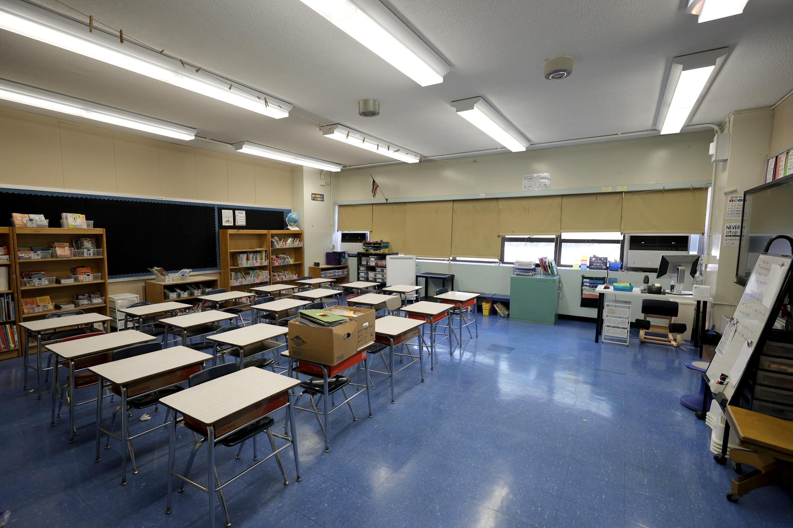An empty classroom with desks, shelves, and a chalkboard