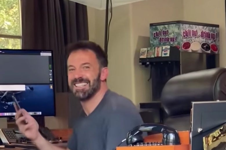 A smiling Ben Affleck in his office. Behind him is a soda machine with both Diet Coke and Diet Pepsi.
