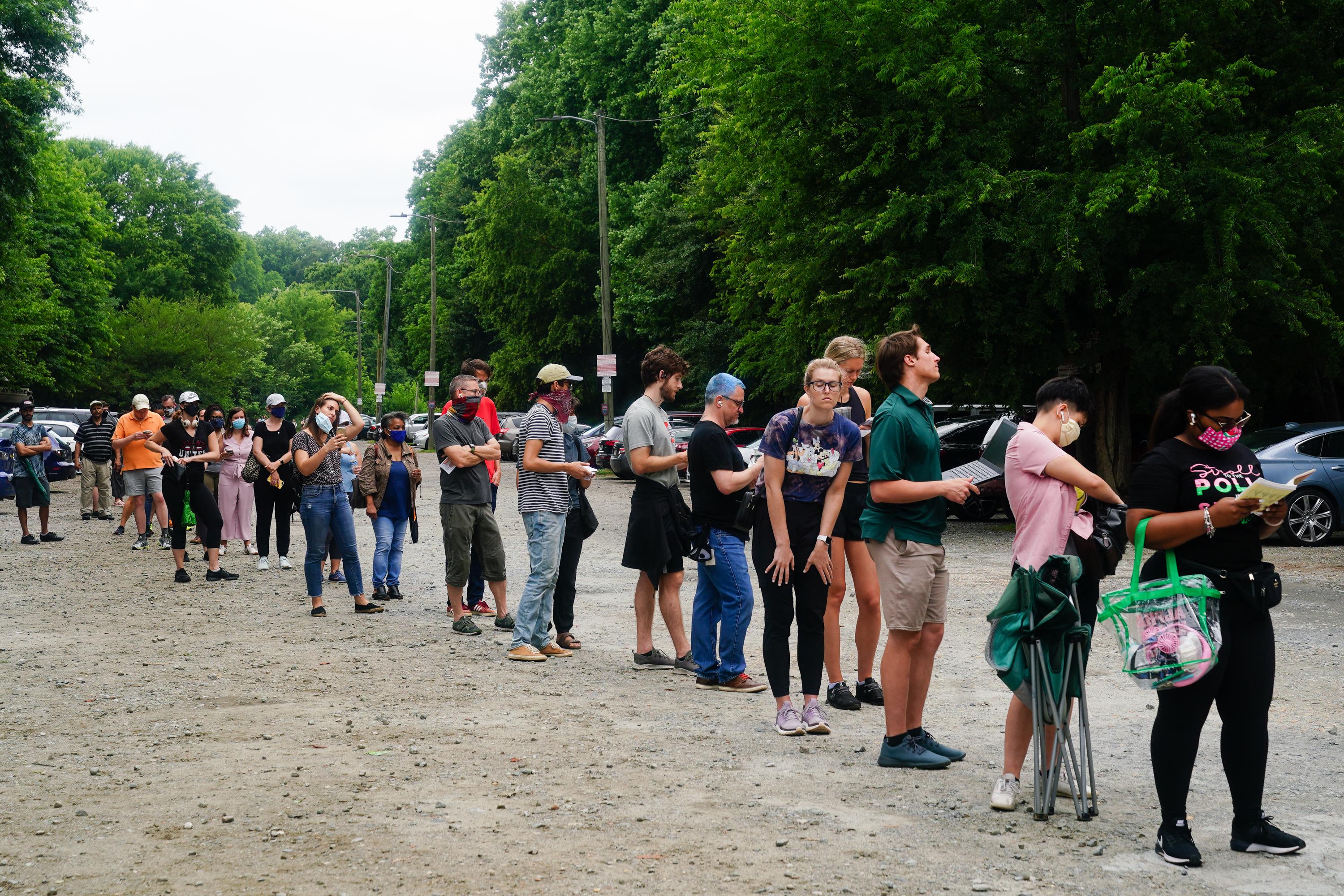 A long line of people standing in a parking lot, with trees in the background