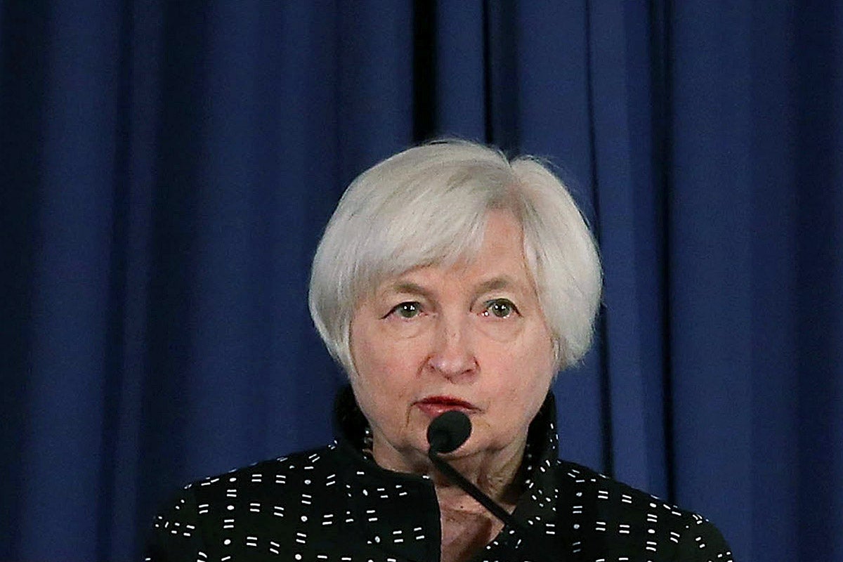 Janet Yellen speaks into a microphone against a blue curtain.