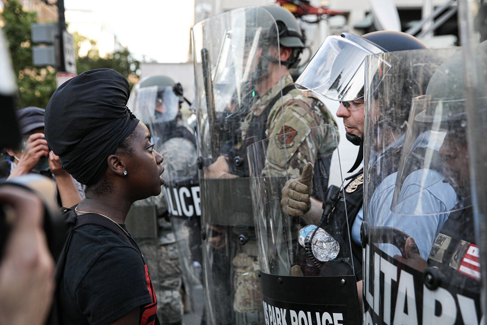 A protester directly faces officers who are carrying shields and blocking the road.