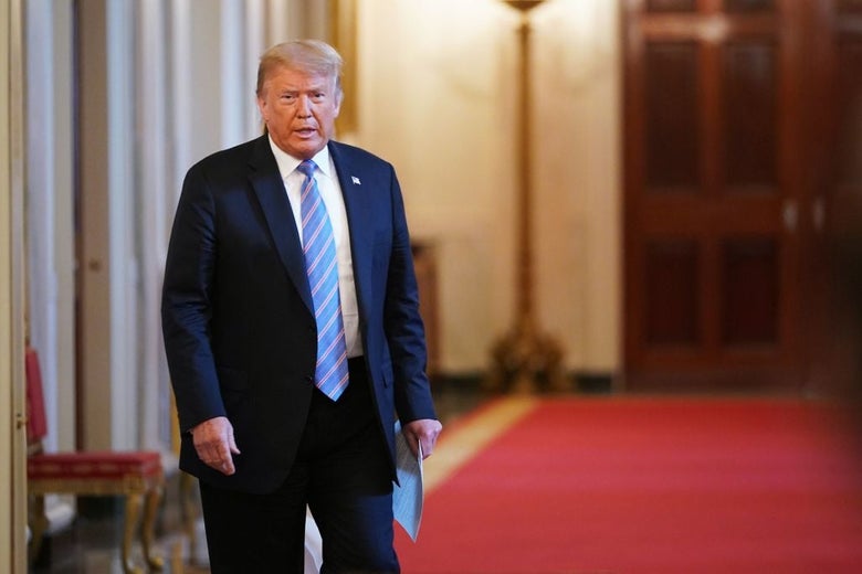 Trump walks around a corner in a red-carpeted hallway.
