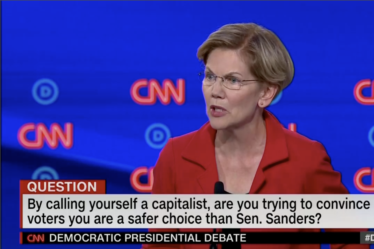 In this screengrab from CNN, Elizabeth Warren debates. The banner reads: "By calling yourself a capitalist, are you trying to convince voters you are a safer choice than Sen. Sanders?"