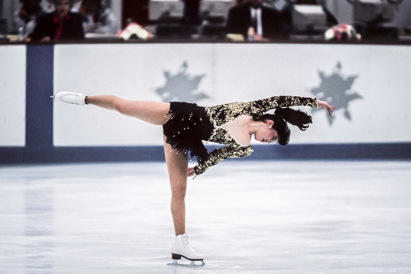 Yamaguchi skates on one leg with her arms and other leg parallel to the ground. She's wearing a black dress.