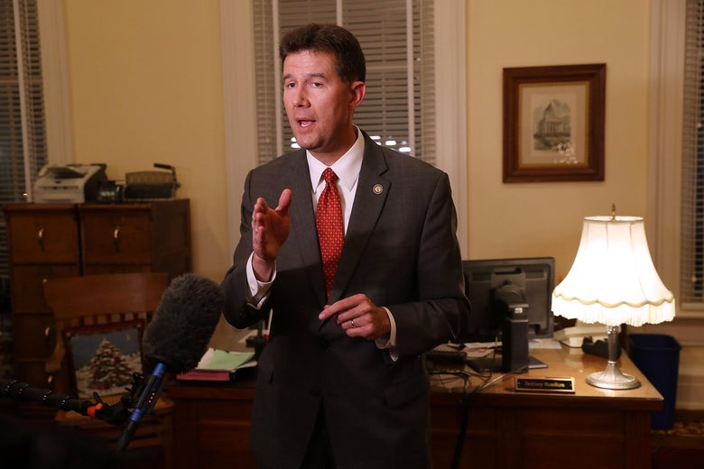 John Merrill speaks to TV cameras in front of a Christmas tree.