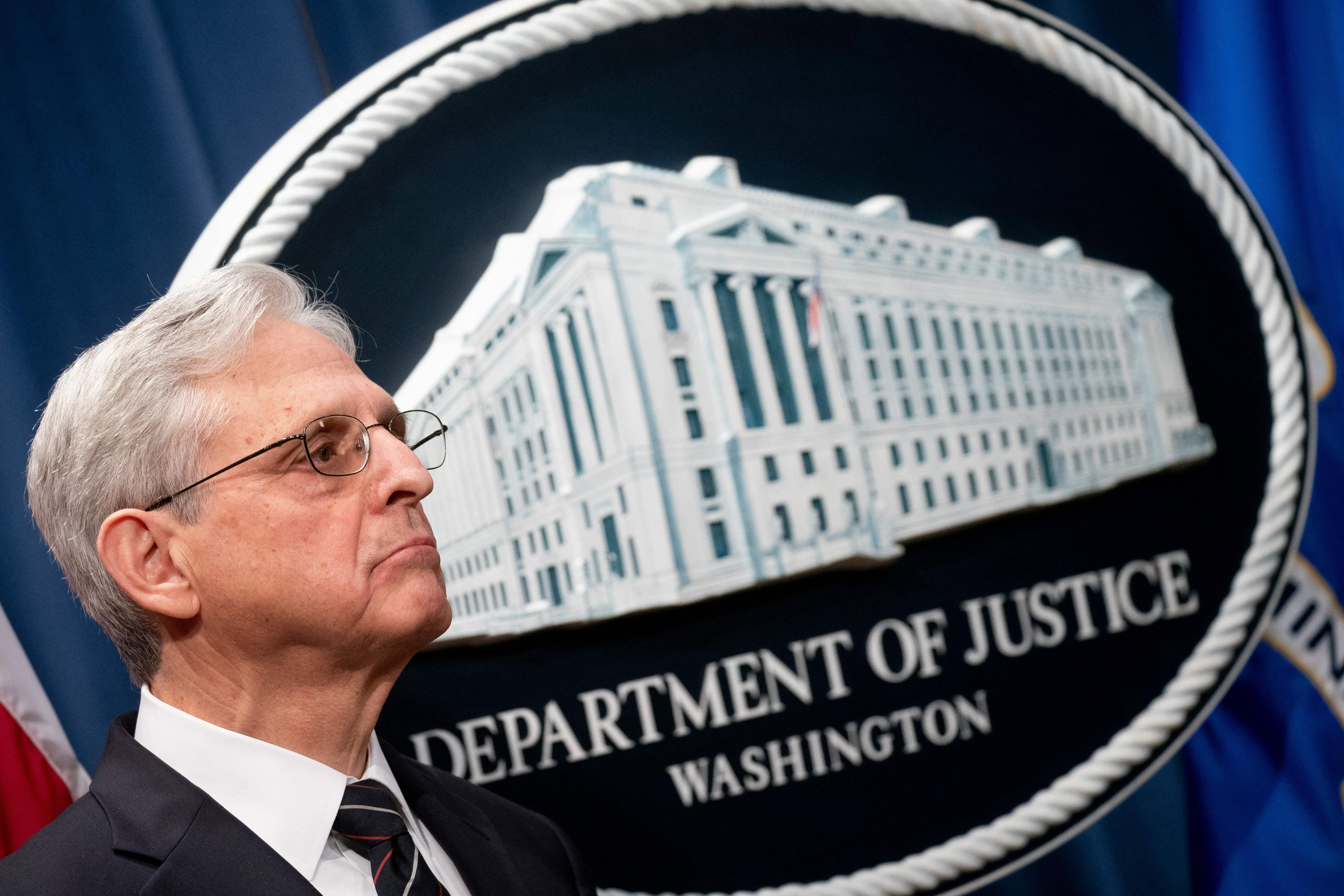 A man in a suit stands in front of a Department of Justice seal.