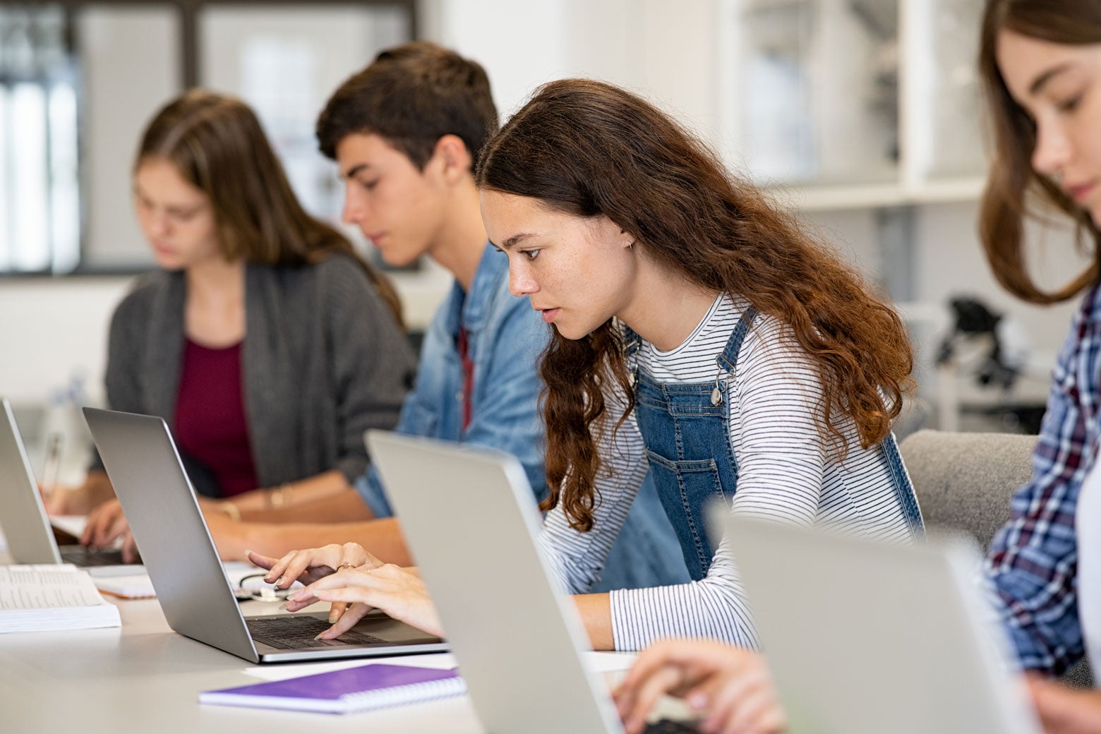 Several teen students look intently at their own laptops.