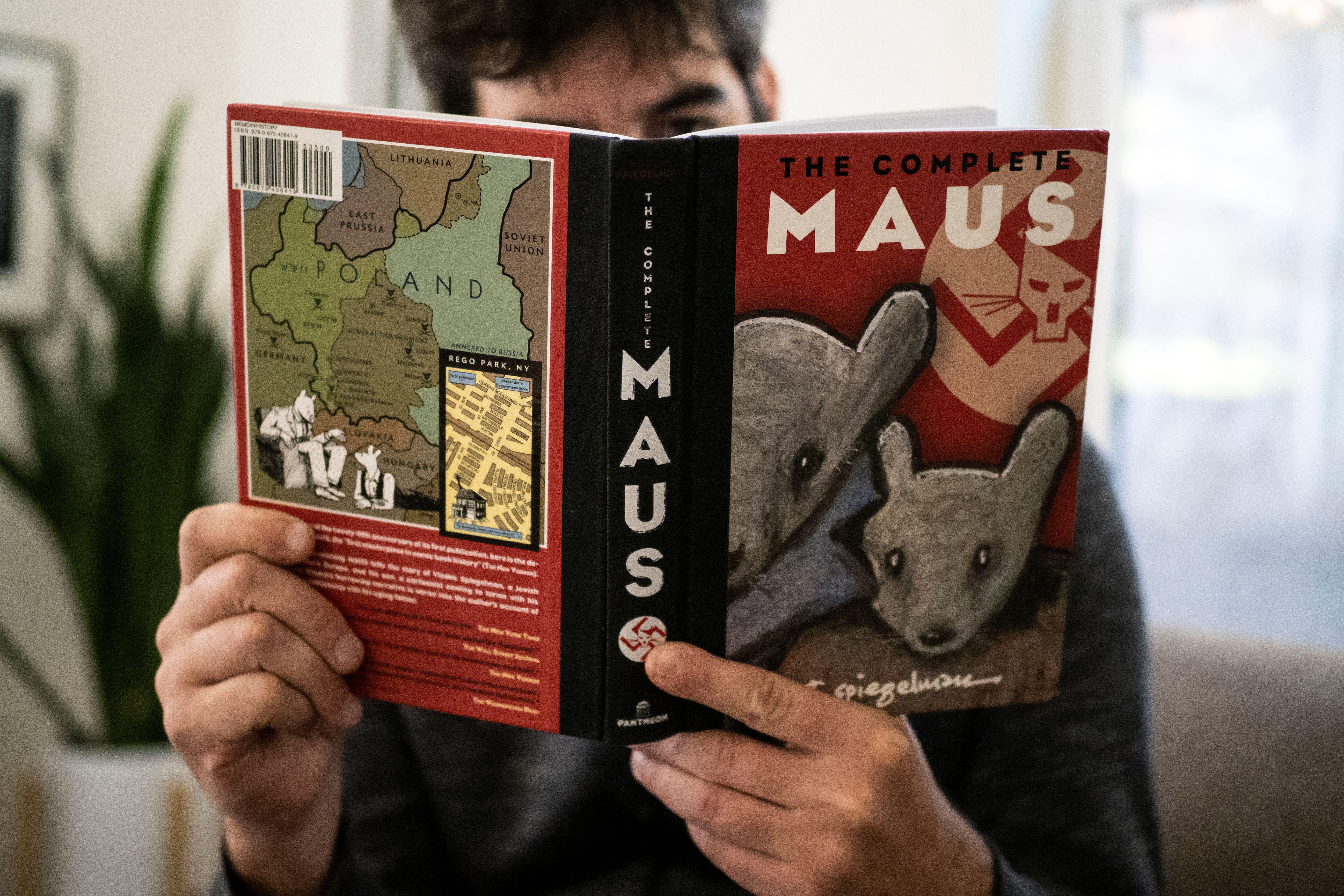 A person's hands holding up the book, Maus, with the front cover featuring a pair of mice and a swastika