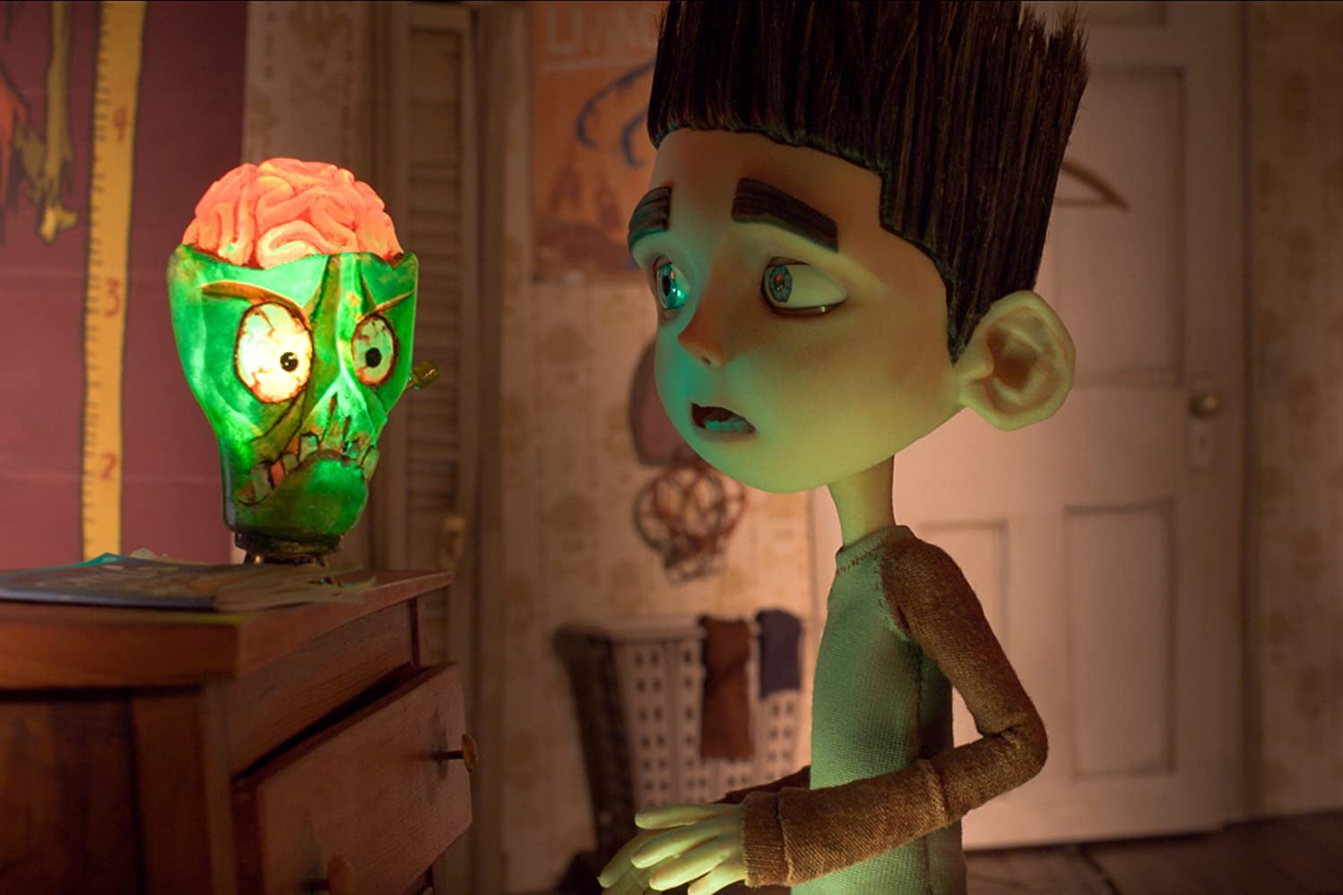 Norman Babcock looks at a glowing green skull lamp with an exposed brain.