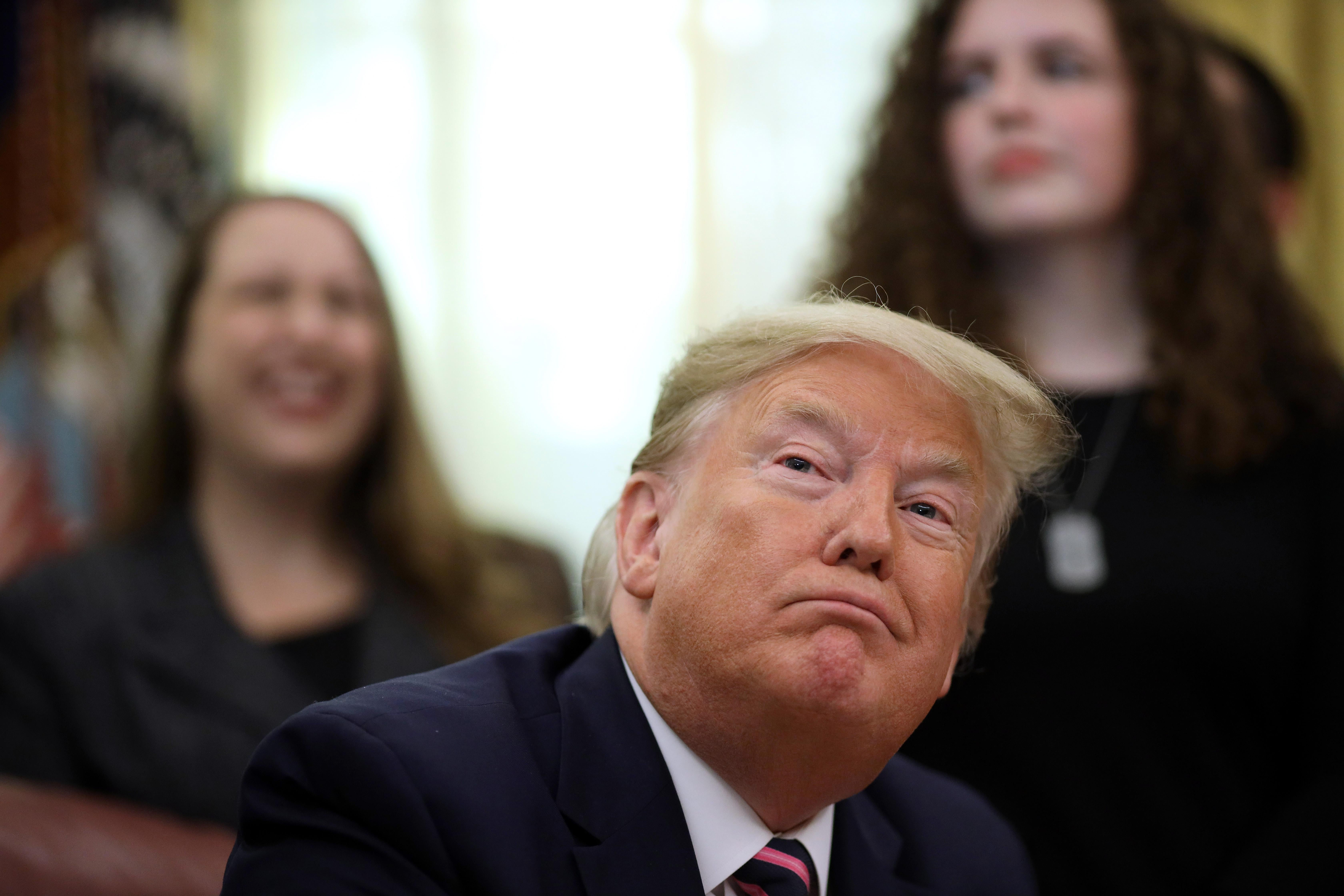 Trump seated, with students in the background.
