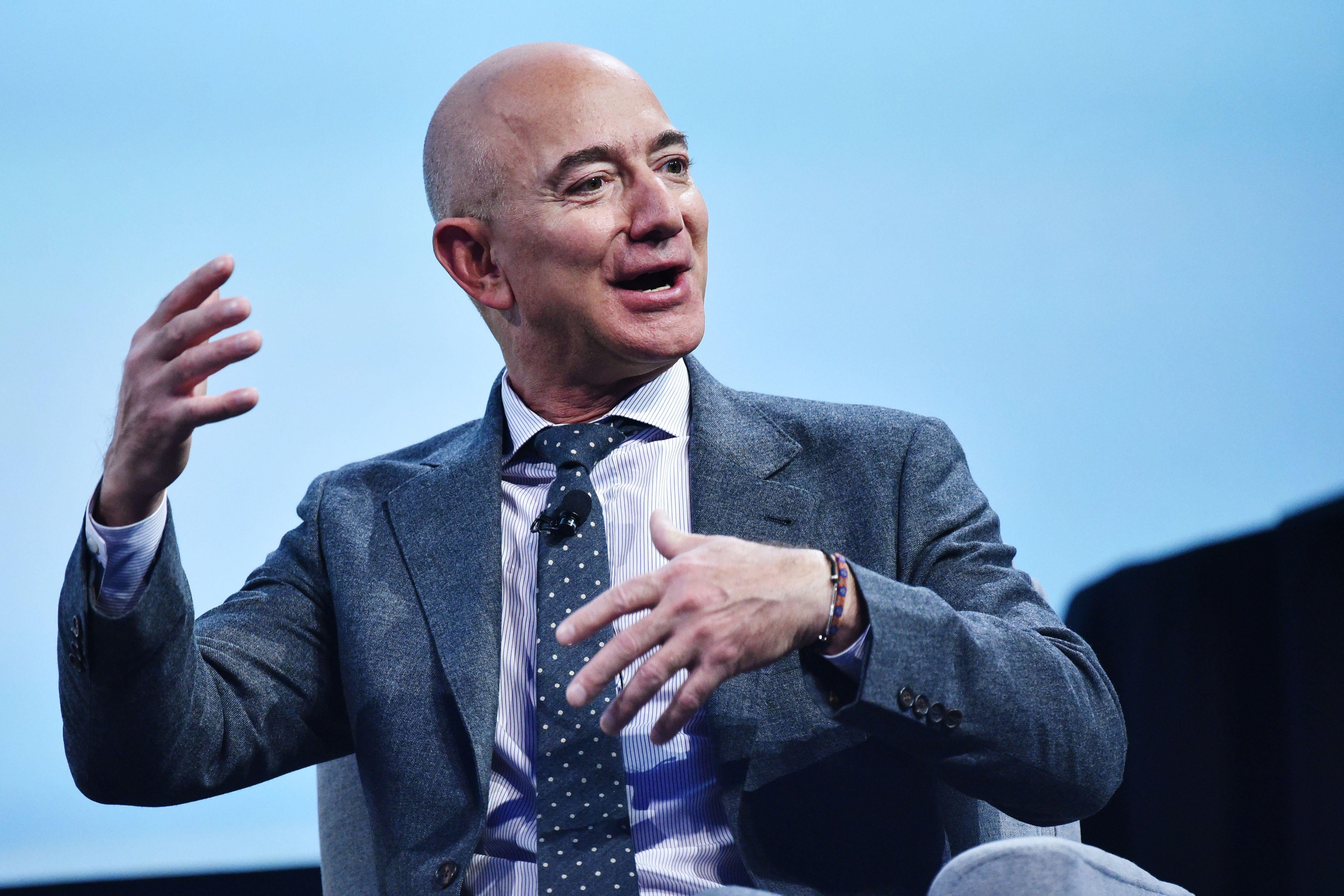 Jeff Bezos gestures with both hands while sitting in front of a light-blue screen.