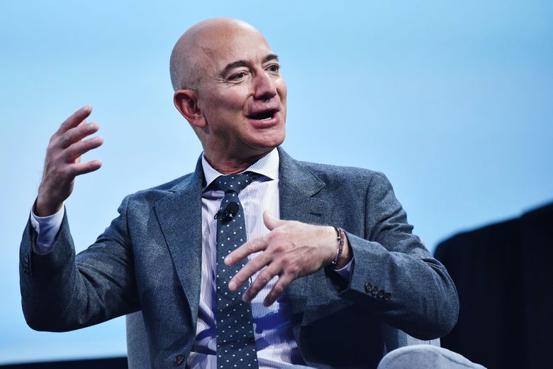 Jeff Bezos gestures with both hands while sitting in front of a light-blue screen.