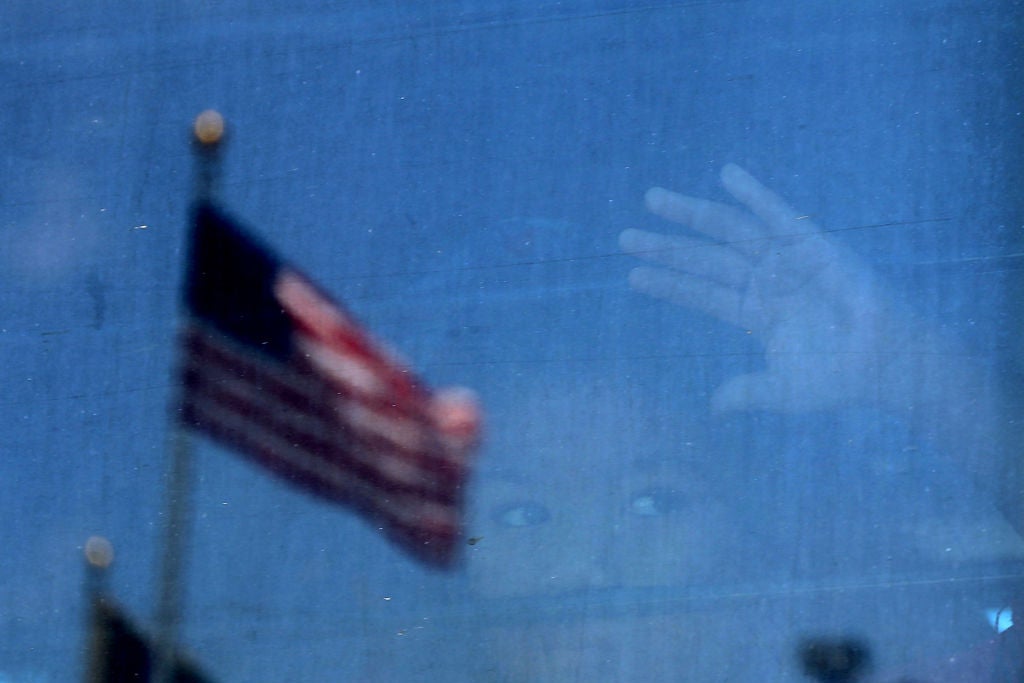 A young child's face can be seen through the window of a bus against which a United States flag is reflected.