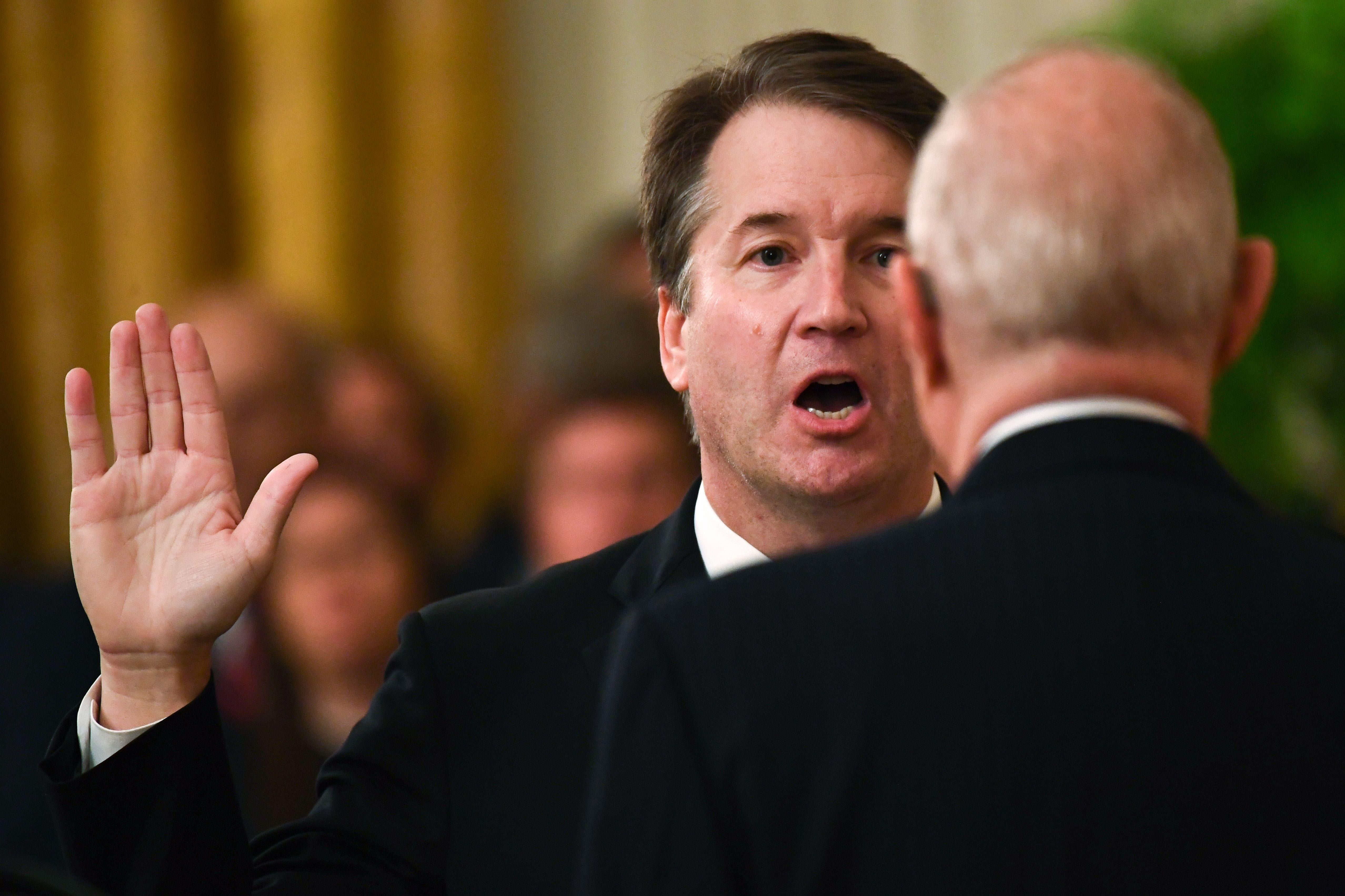 Kavanaugh raises his right hand as he faces Kennedy, who is seen from behind.