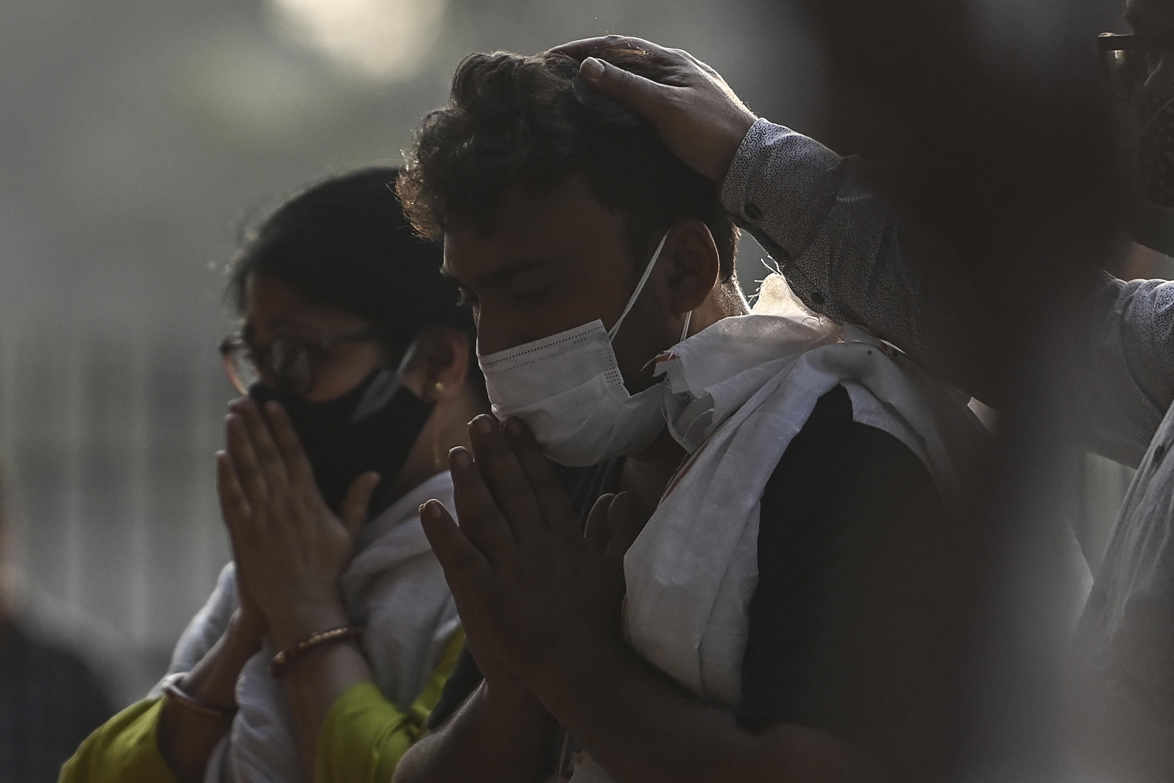 A man and a woman, both wearing masks, hold their hands in prayer to their mouths.