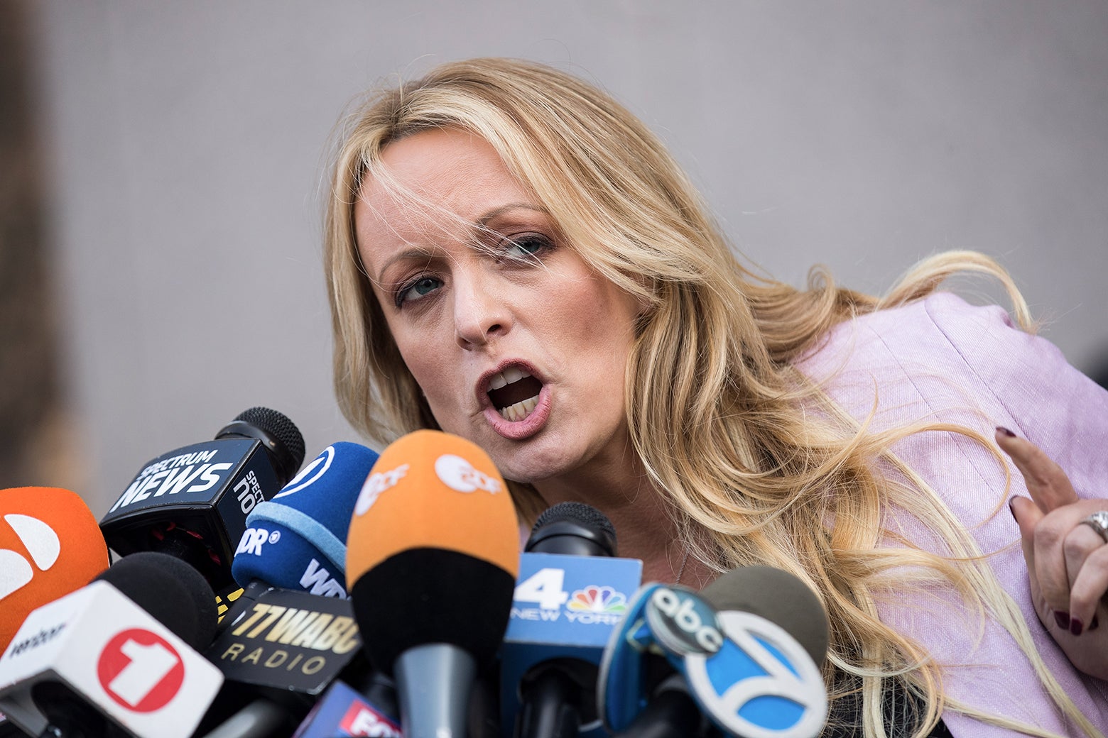 Stormy Daniels pointing and speaking into a scrum of microphones.