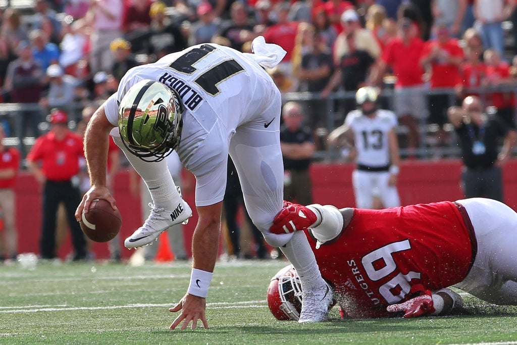 A Purdue quarterback stumbles as a Rutgers defensive lineman laying on the ground holds his left leg.