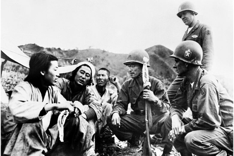 American soldiers crouch down to talk with North Koreans in a historical black-and-white photo.