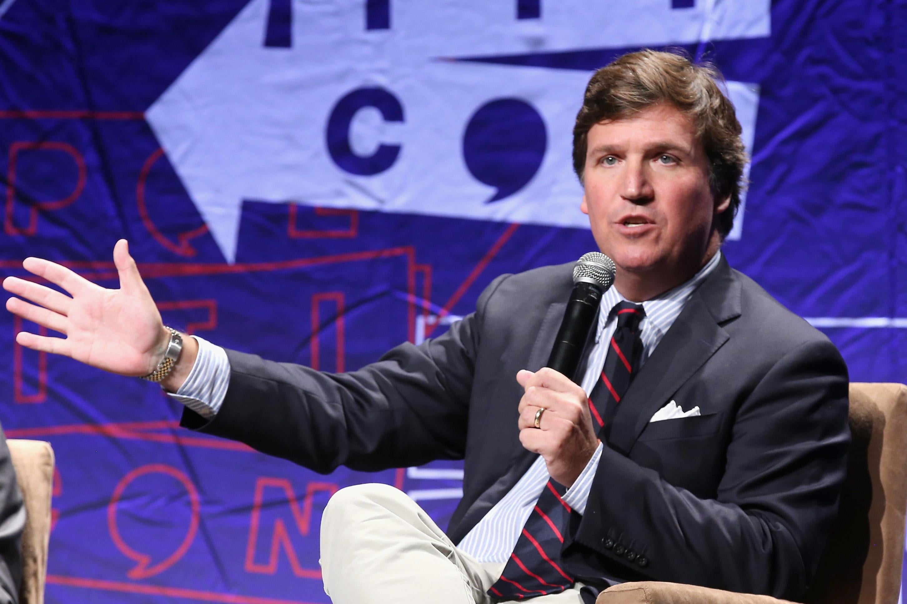 Tucker Carlson speaks into a microphone as he sits on a stage.