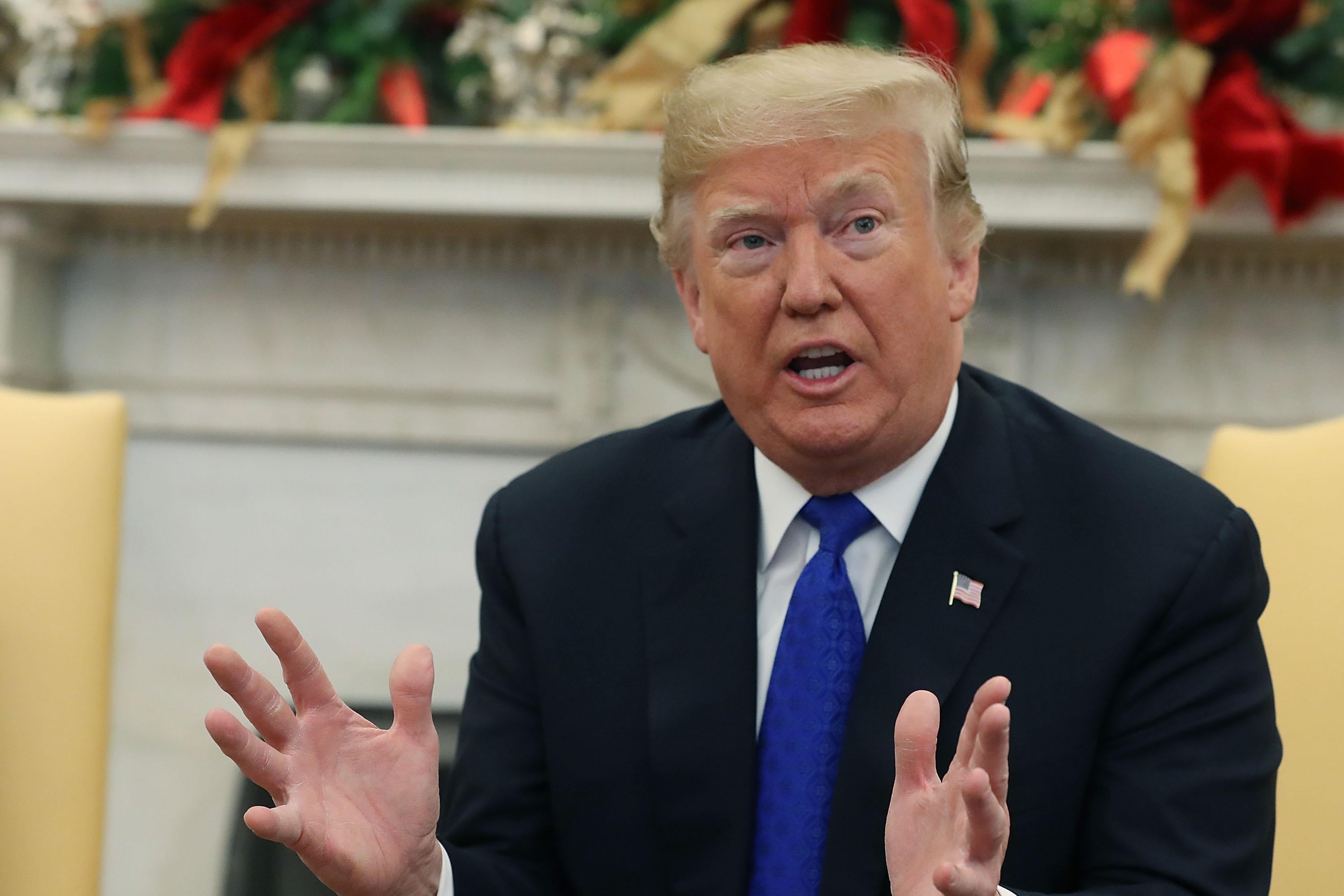 Trump gestures outward with both hands as he speaks. He is seated in the Oval Office, which is decorated for Christmas.