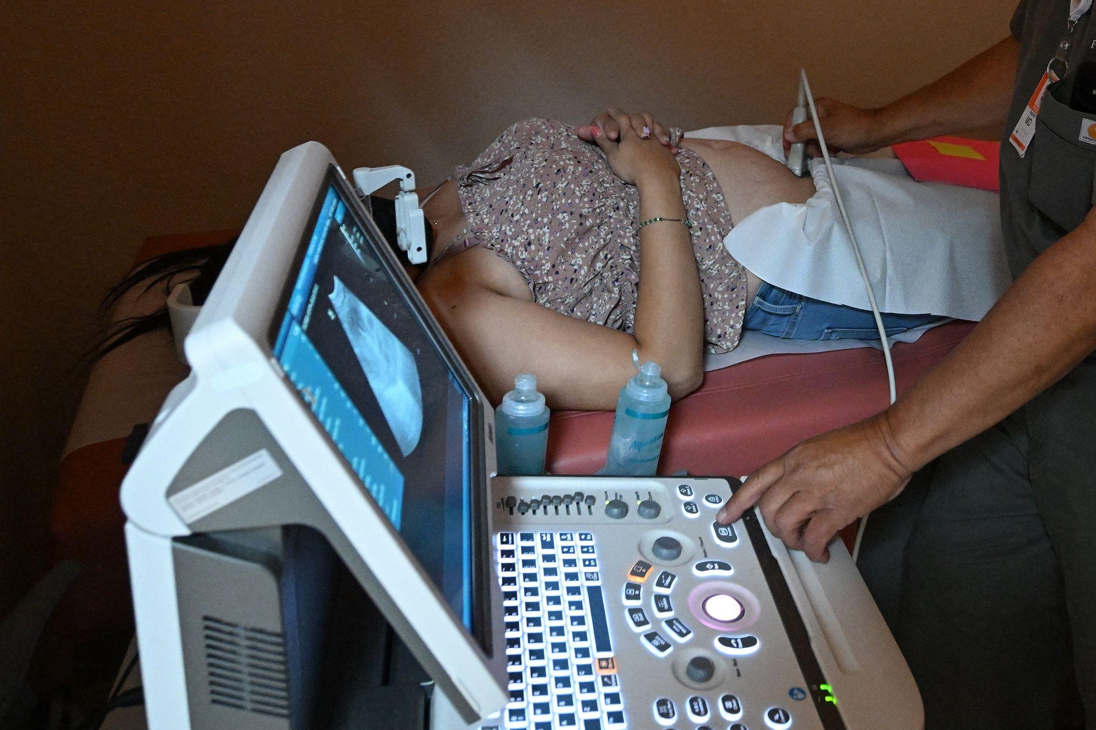 A doctor’s arm on a woman's stomach with one arm, controlling a keyboard and looking at the sonogram on-screen with the other