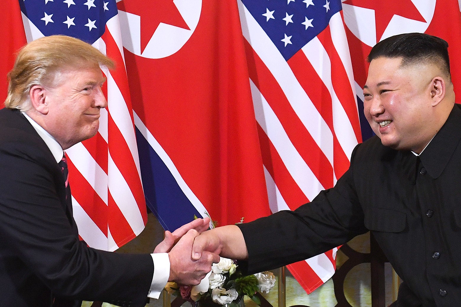 Donald Trump and Kim Jong-un, seated, shake hands.