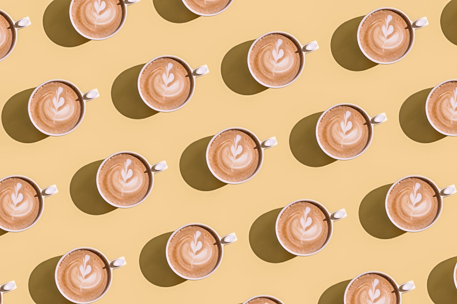 A repeating pattern of a mug with a latte in it against a light yellow background.