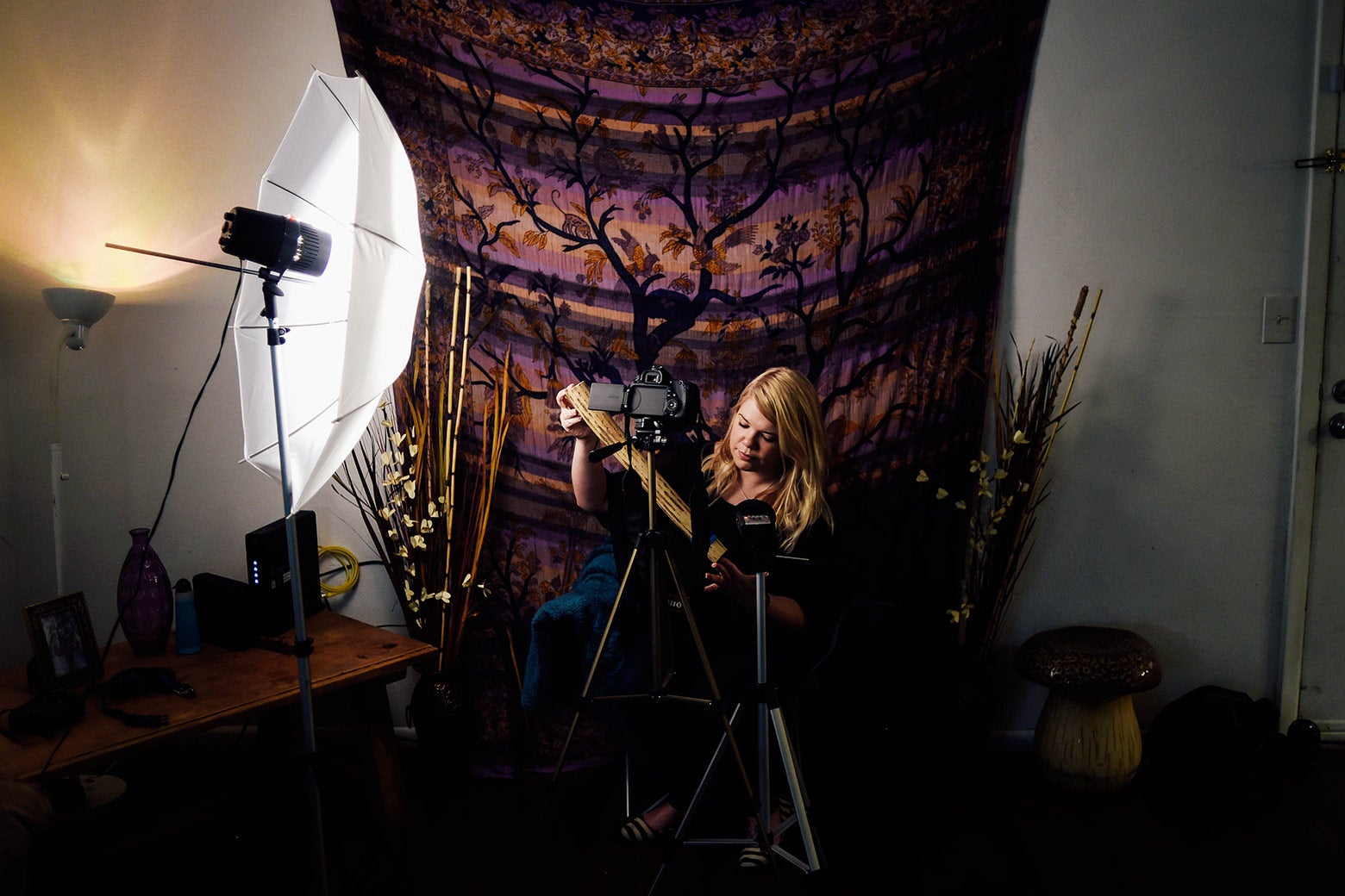 A woman holds a rainstick with a camera and lighting gear pointed toward her.