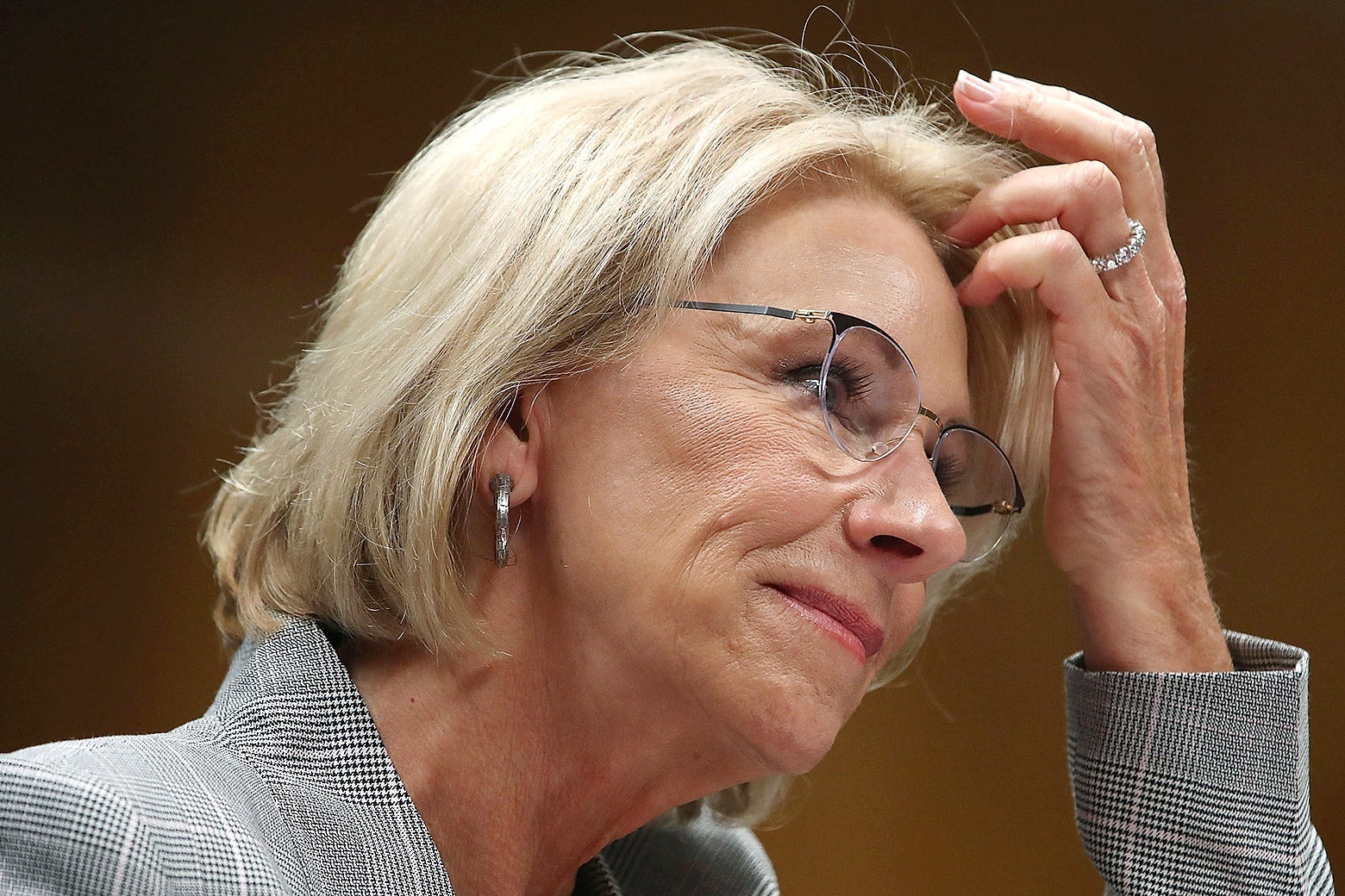 Betsy DeVos adjusting her hair at a hearing.