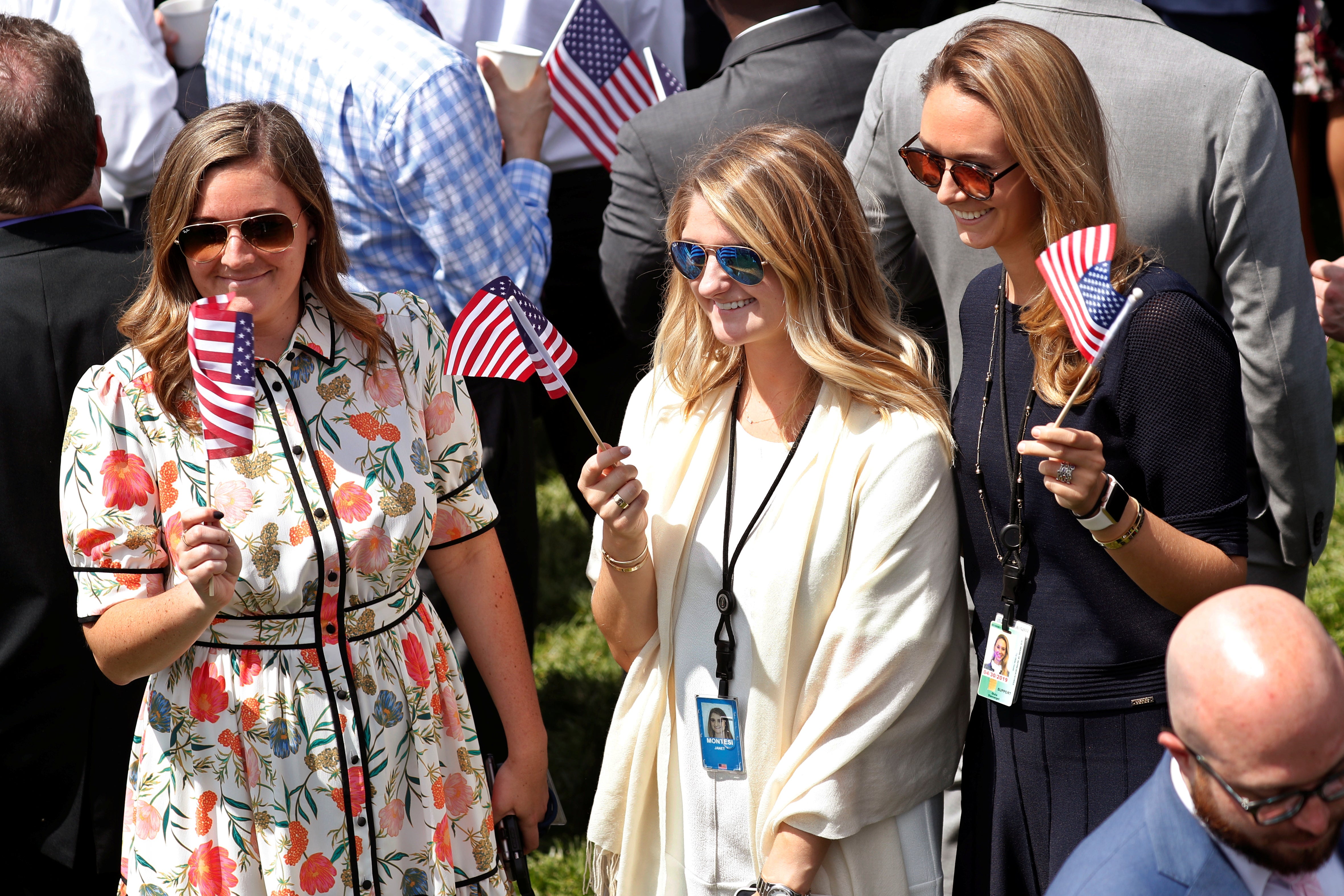 Three young women in professional dress, two of whom are wearing ID badges, wave miniature flags.
