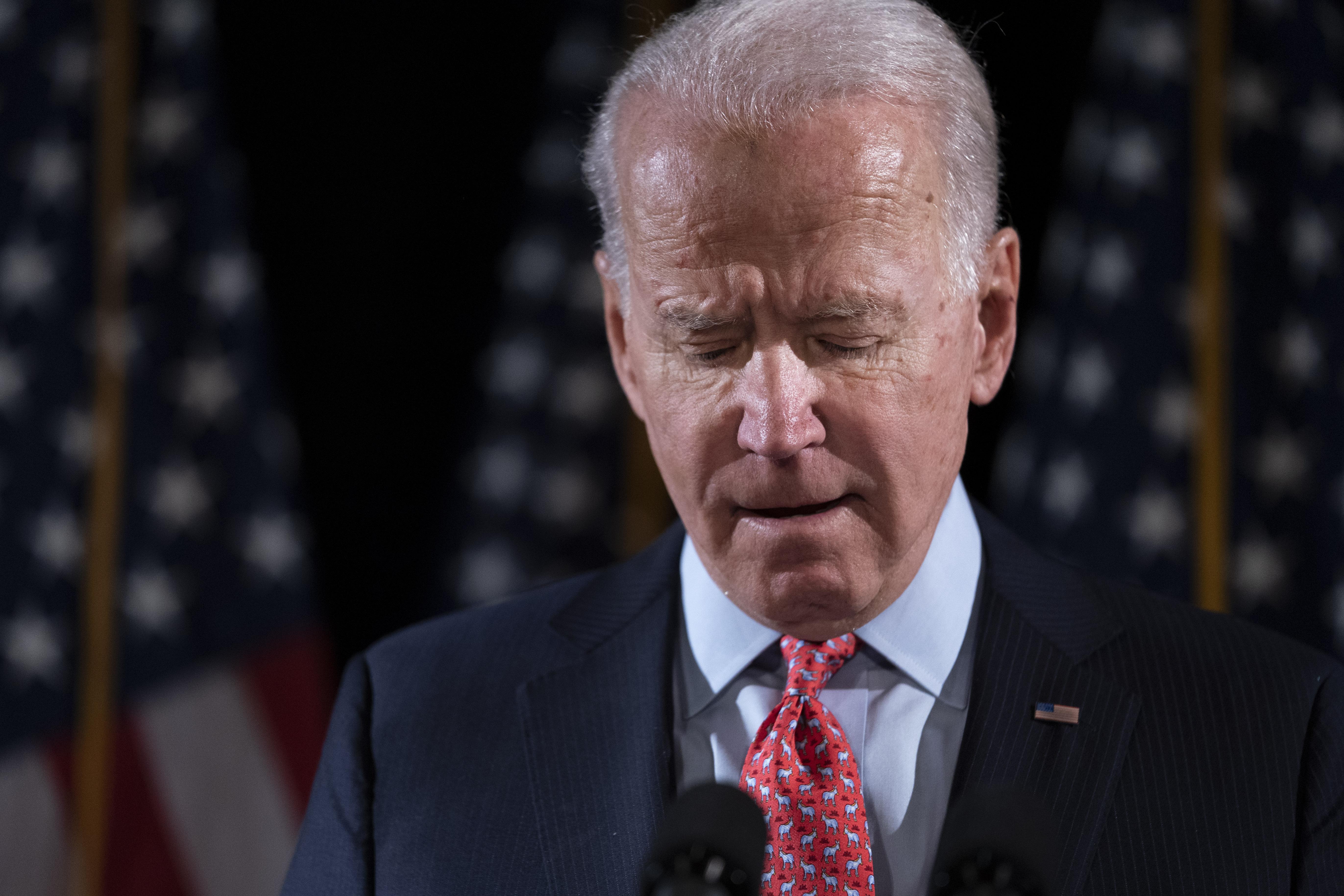 Biden speaks onstage at a mic, looking down with his eyes closed.