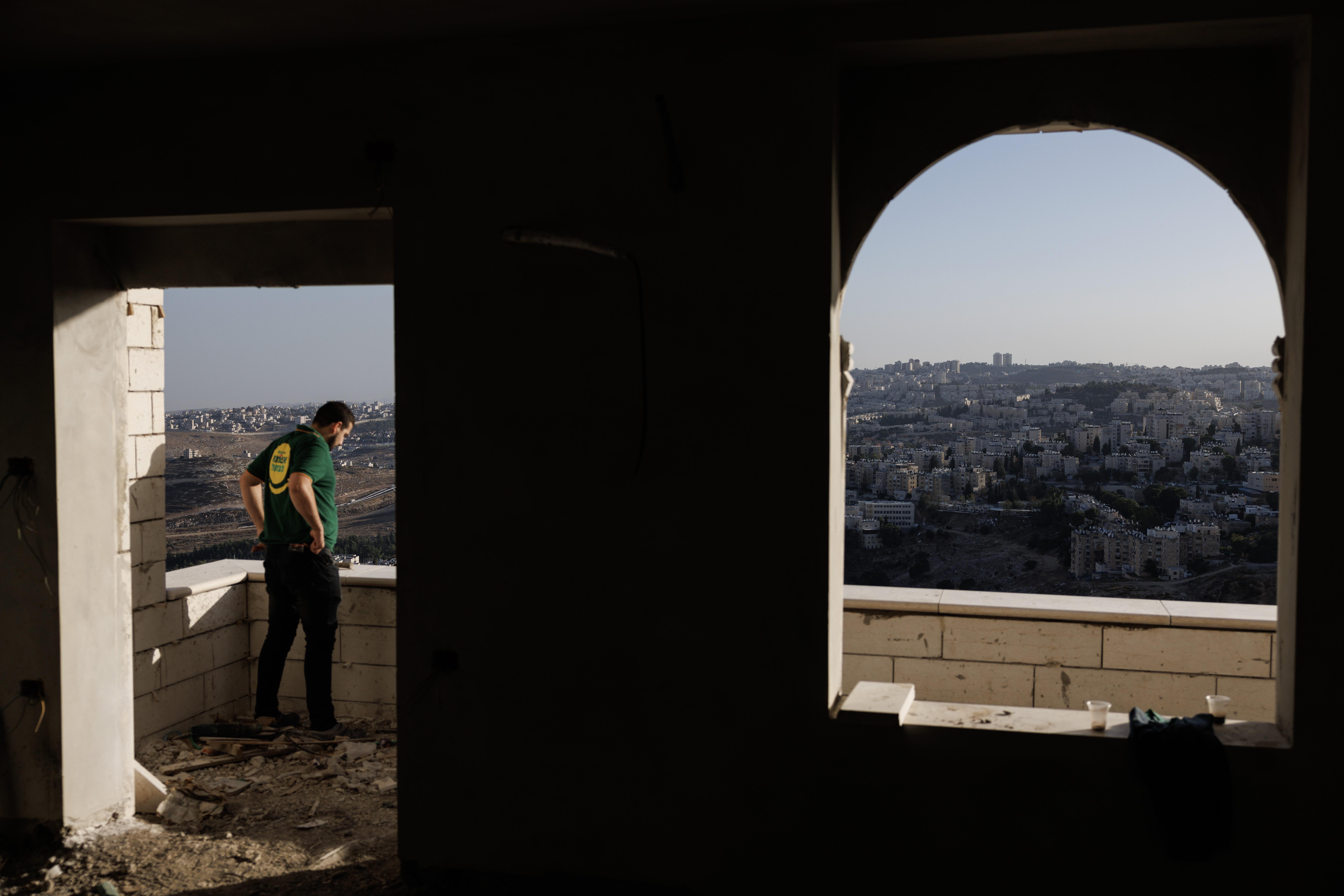 A man stands in the opening made by the doorway of a building overlooking the West Bank.