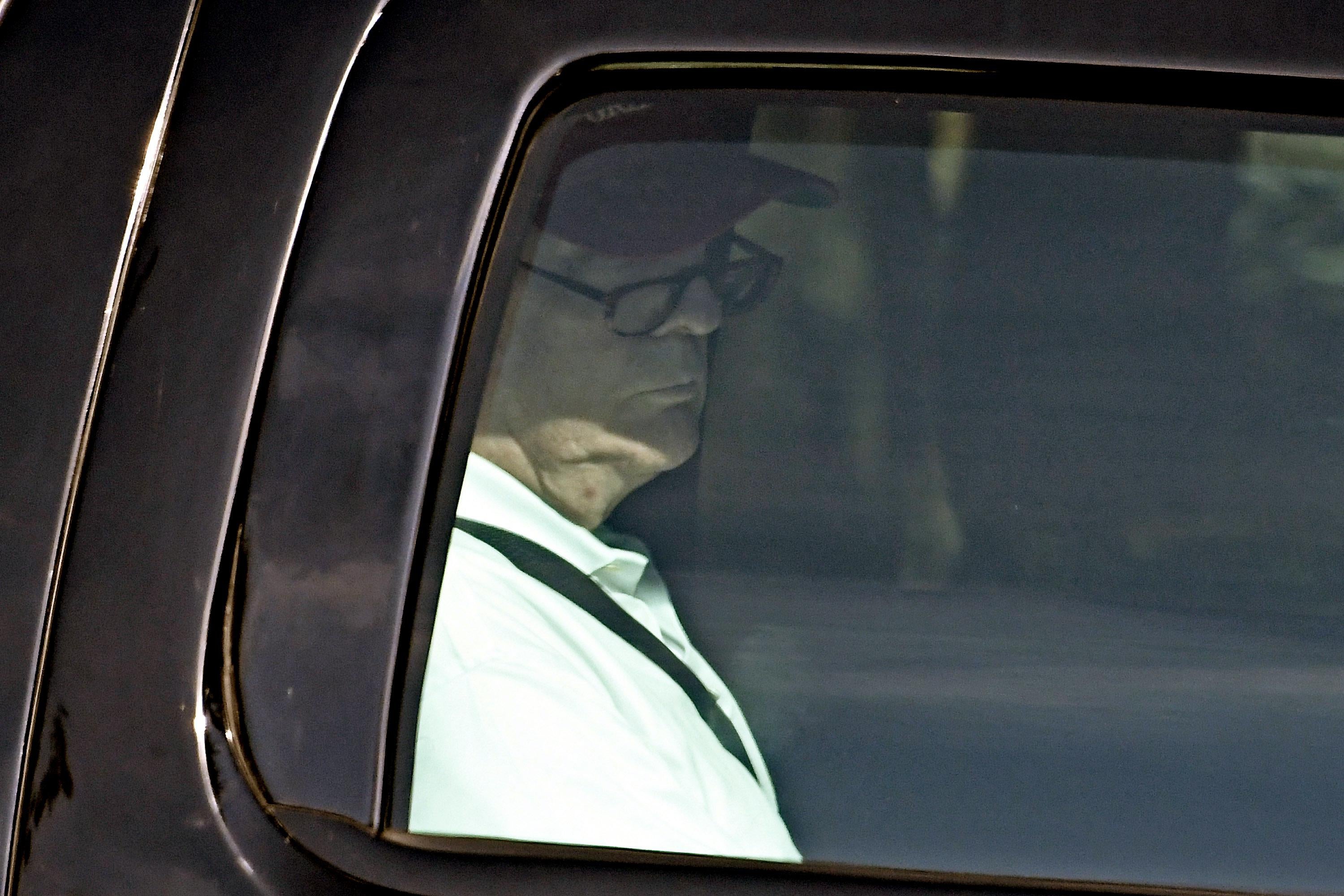 A photograph taken through Donald Trump's limo window shows him wearing glasses as he reads something out of frame.