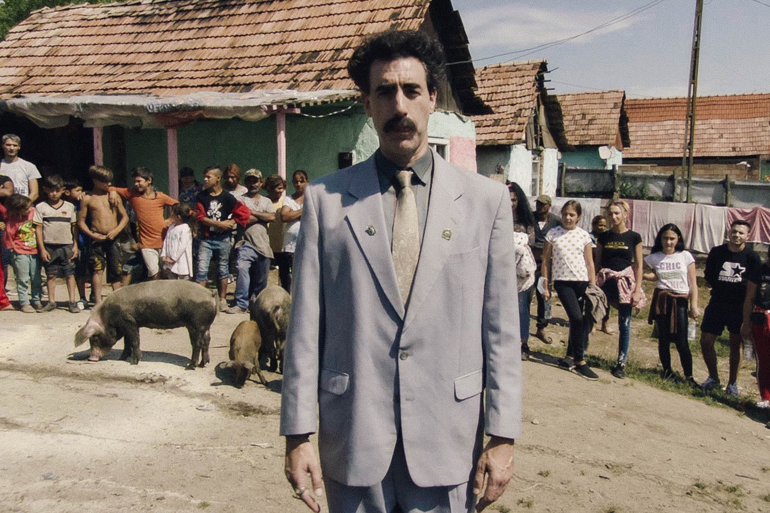 The actor looks very nice in his signature gray suit and Groucho Marx mustache, standing in front of a group of kids in a village