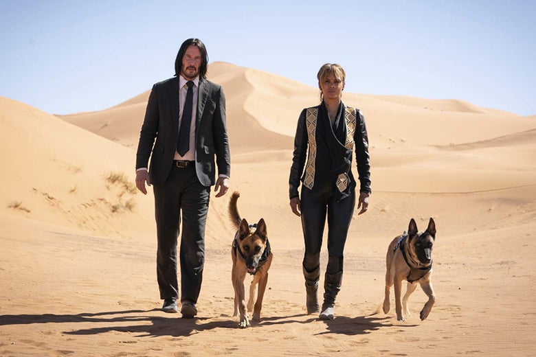 Keanu Reeves, Halle Berry, and two dogs striding across a desert.