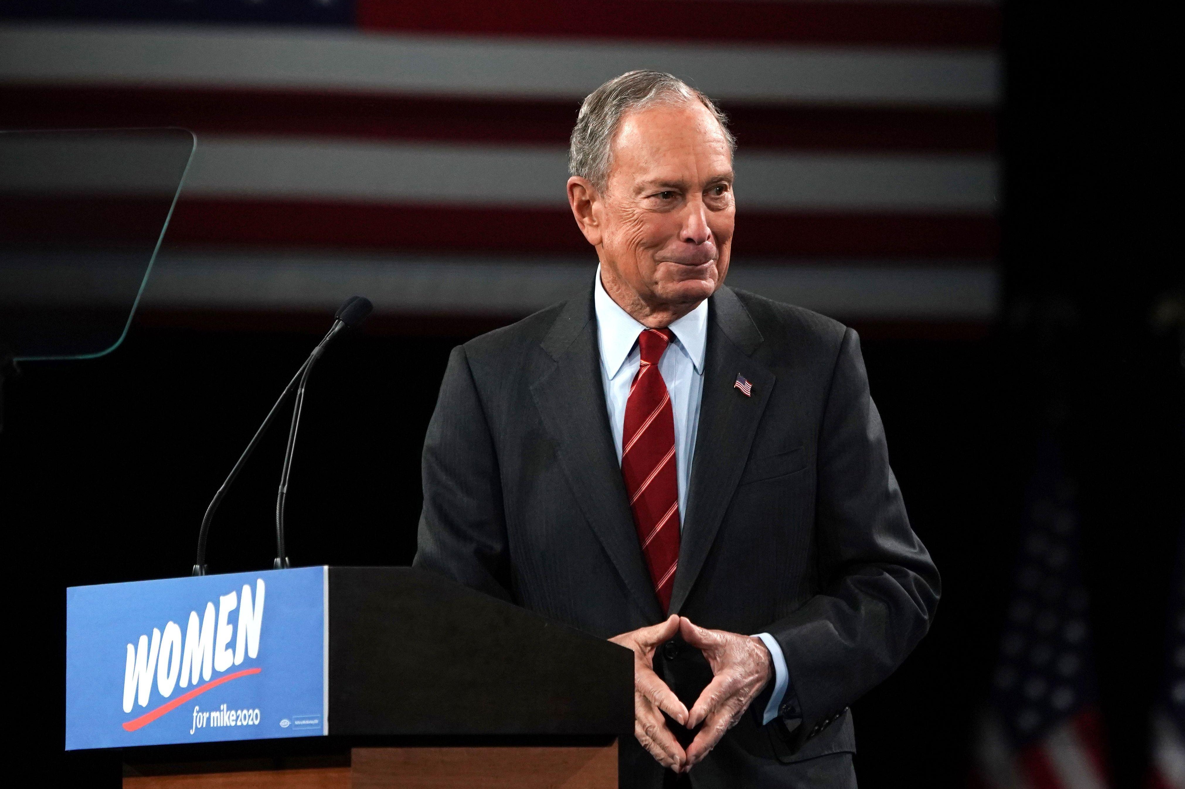 Mike Bloomberg stands in front of a sign that reads "Women for Mike Bloomberg."