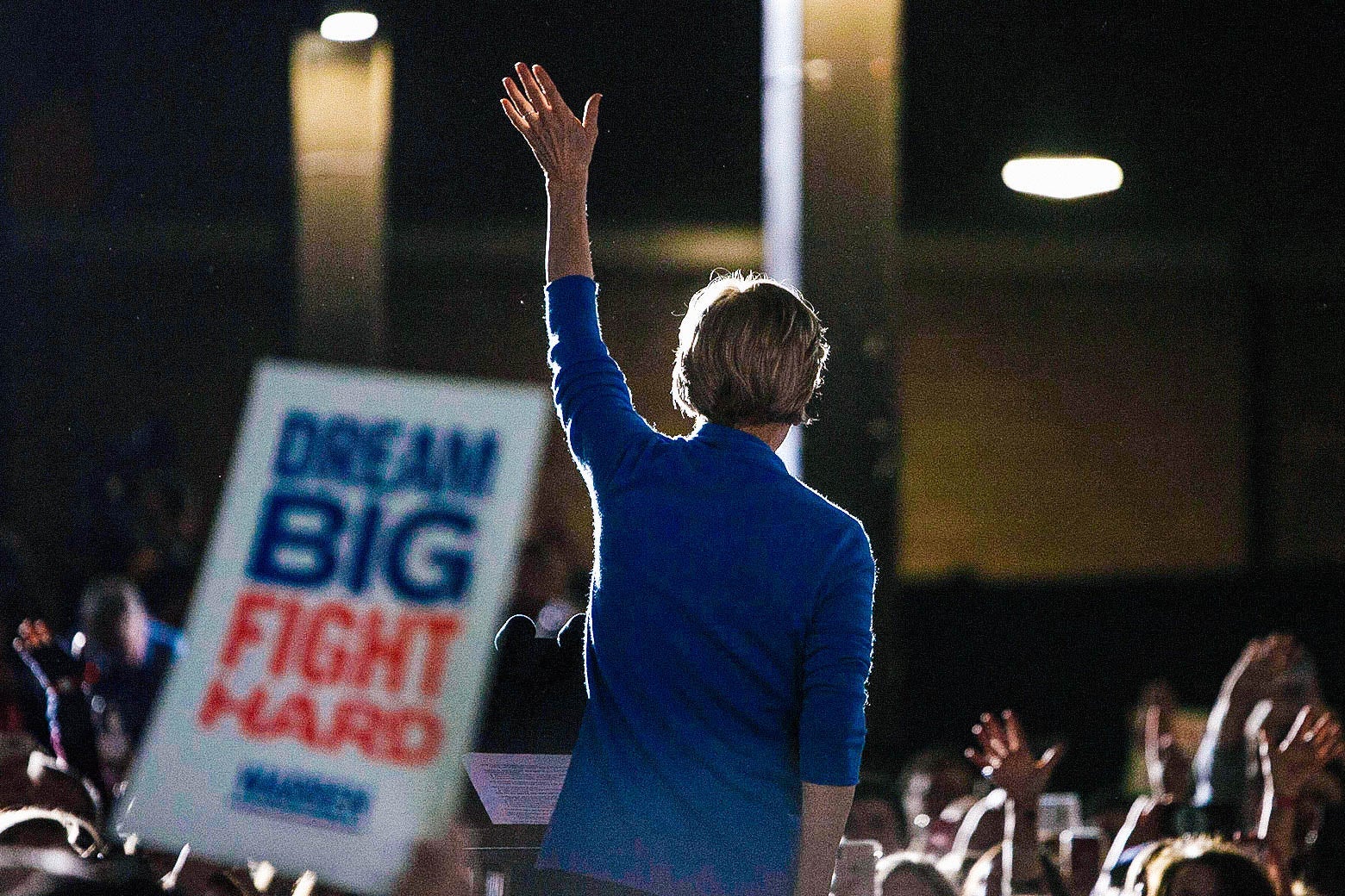 Sen. Elizabeth Warren waves to supporters at a rally, back turned.