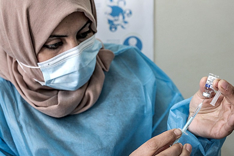 A woman in a headscarf and surgical mask draws a vaccine into a needle from a vial.