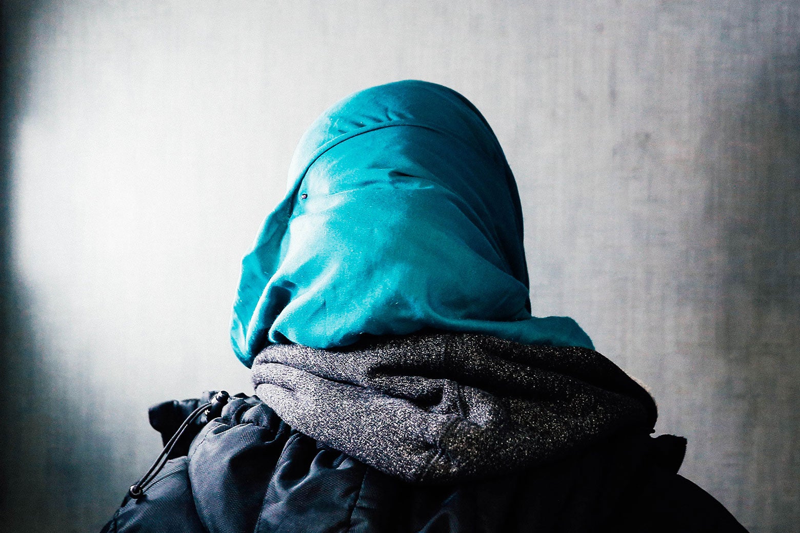 The back of the head of a woman wearing a headscarf, hoodie, and jacket.