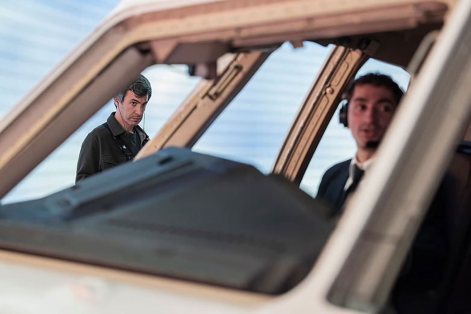 Nathan Fielder watching a twentysomething male co-pilot sitting in the cockpit of a test plane.